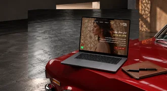 The Roshan Masr website on a laptop resting on a red classic car.